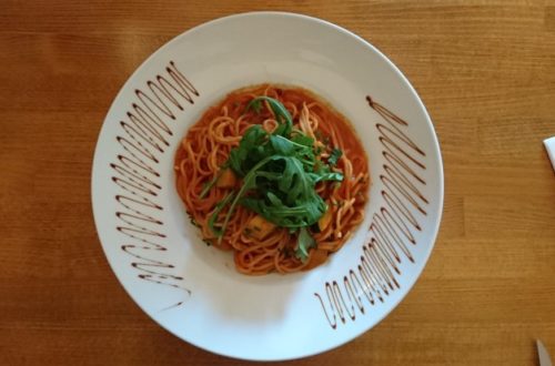 Veganes Spaghetti-Gericht mit Rucola auf weißem Teller von oben