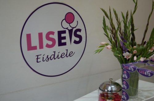 LISEIS Logo an weißer Wand mit Blumen davor